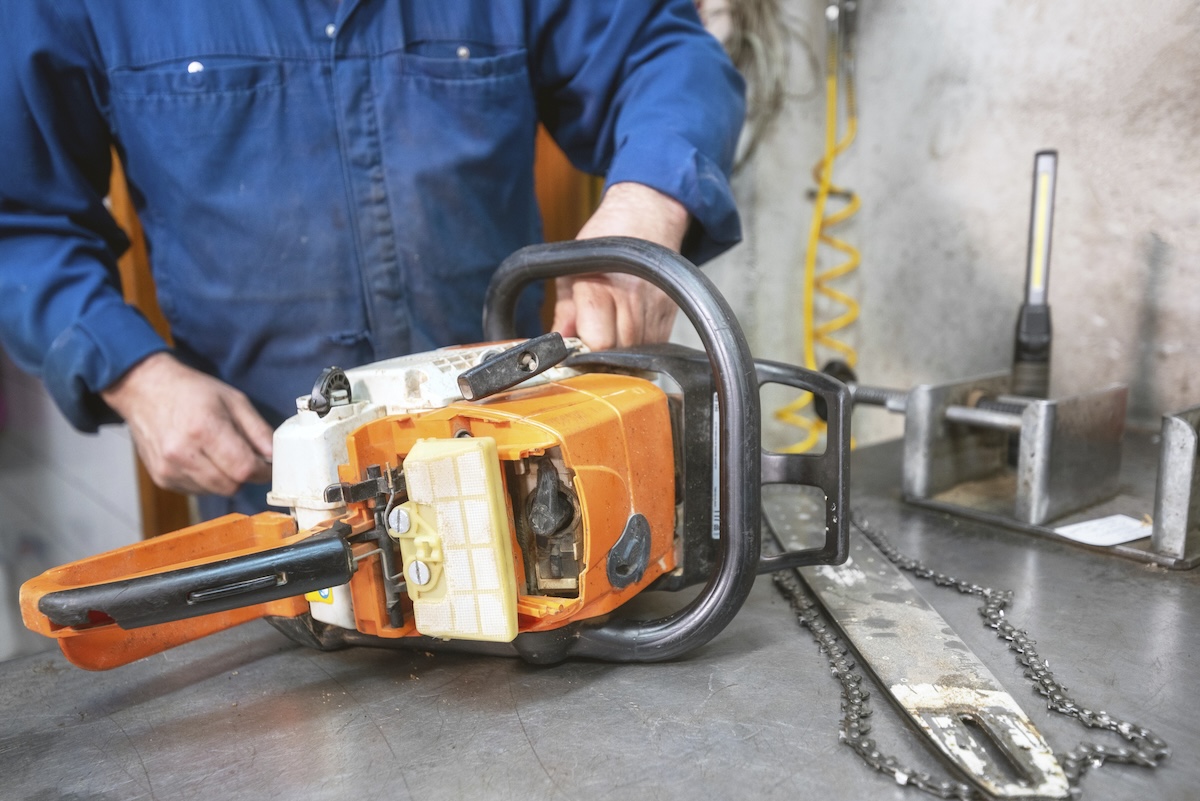 A man in a denim shirt repairs an orange chainsaw.