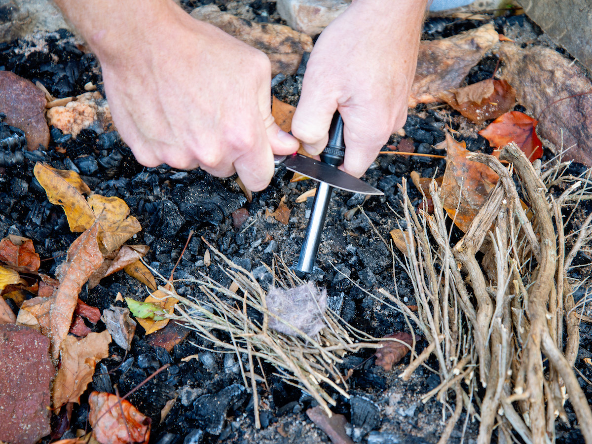 A person is using a tool to start a fire in a fire pit.