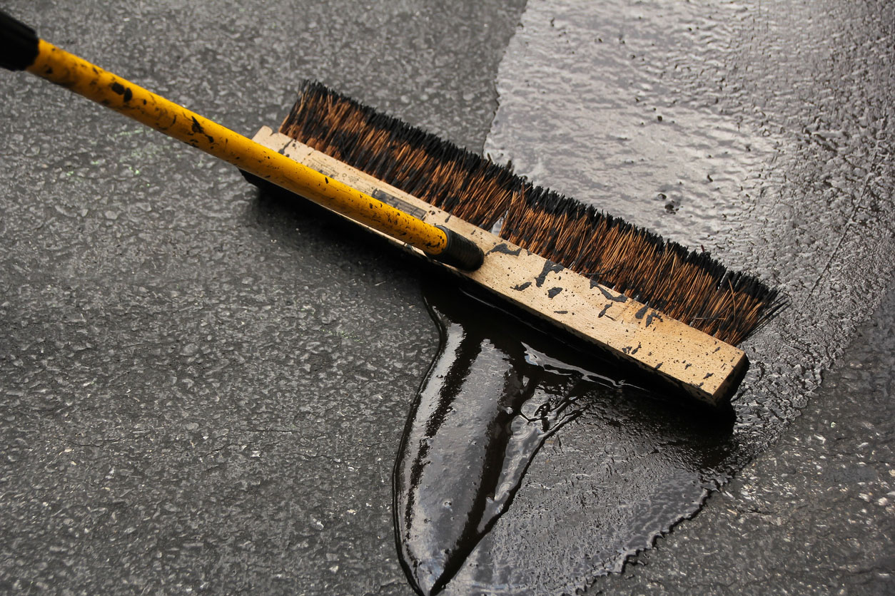 A close up of a brush used to seal a drivewya.