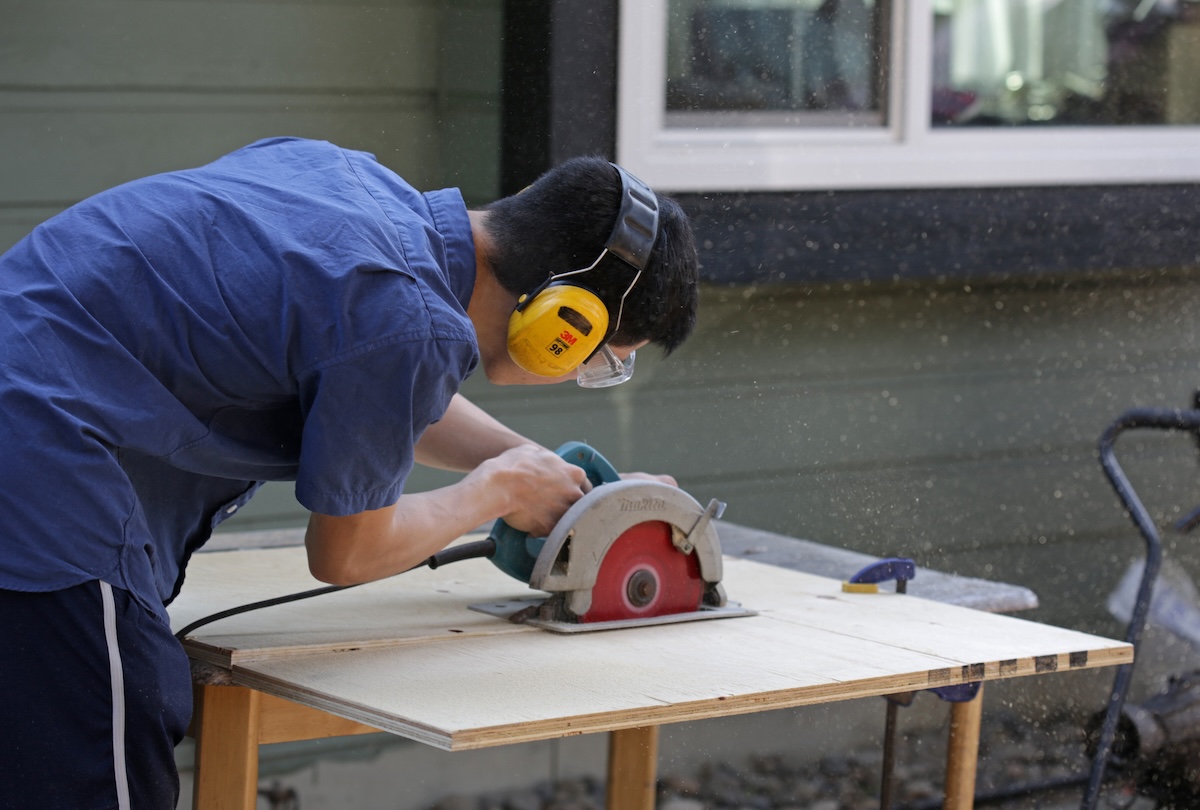 A person using a circular saw to make a rip cut on a sheet of plywood.