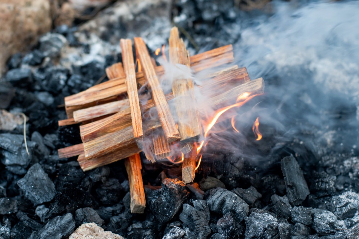 Kindling in a cross structure is burning in a fire pit outdoors.