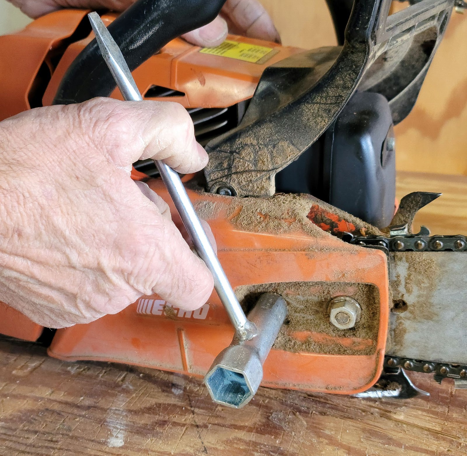 Person uses a scrench to loosen the casing on a chainsaw.