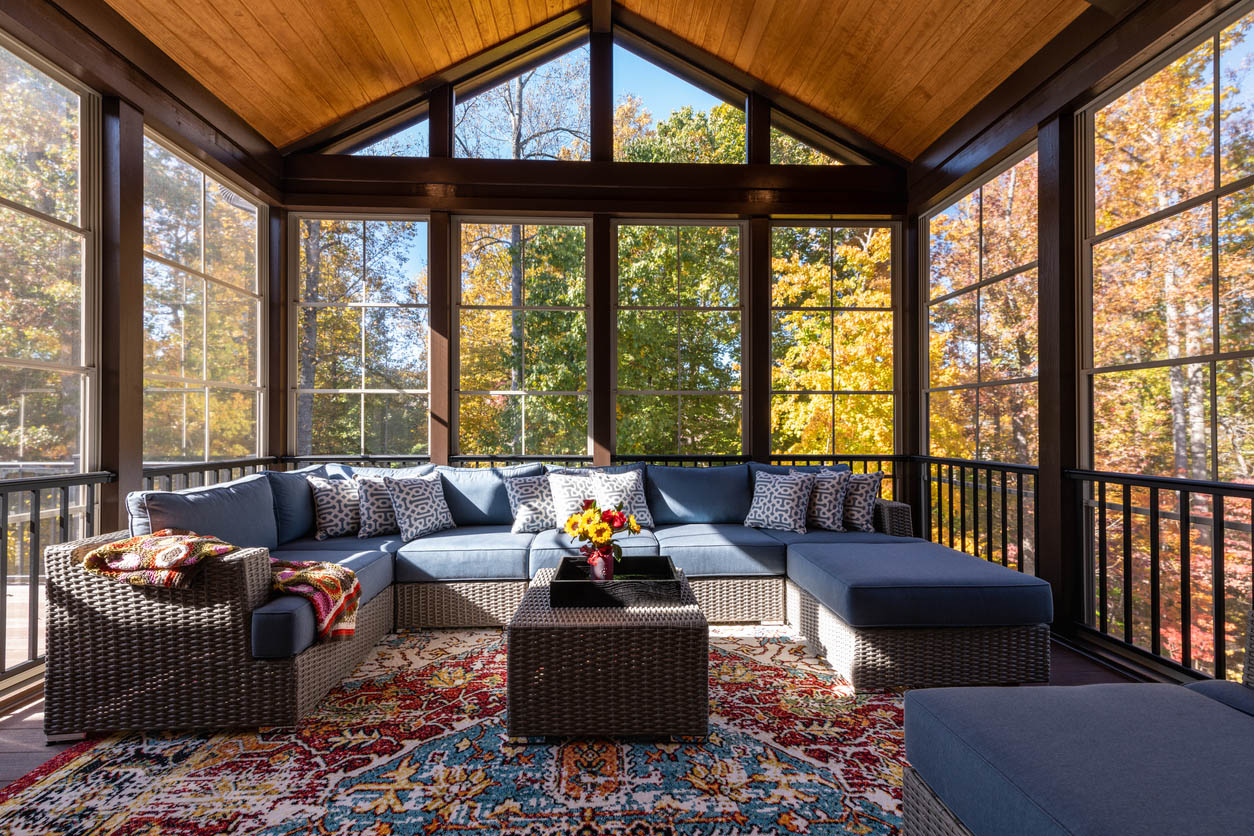 An interior shot of a sunroom decorated with a patterned rug and an outdoor patio furniture set, with fall trees in the background.