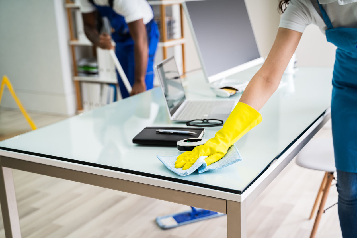 A close up of a cleaner's gloves hand wiping down a desk.