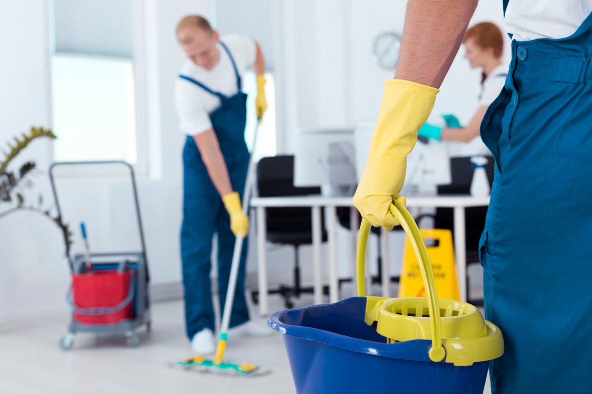 A team of cleaners in blue overalls and yellow gloves clean an office space.