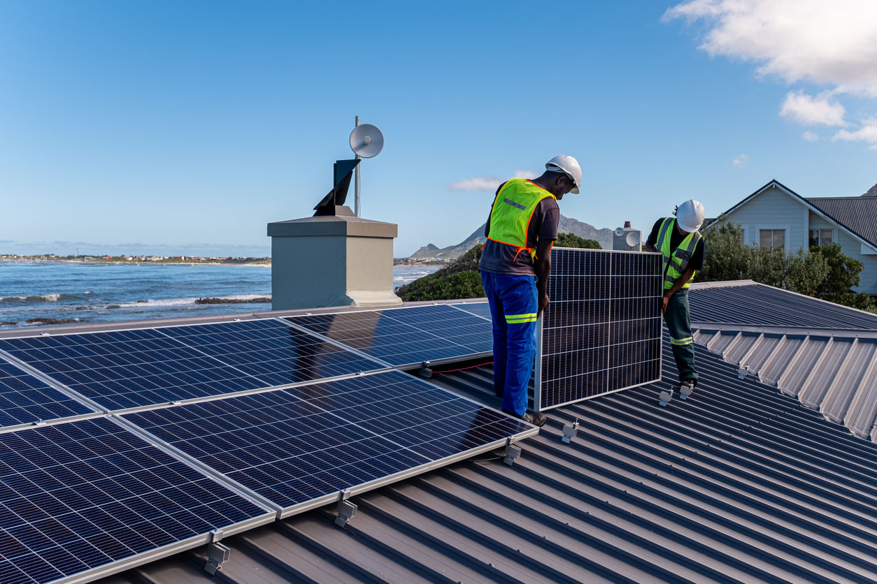 Two workers install solar panels on a roof. 