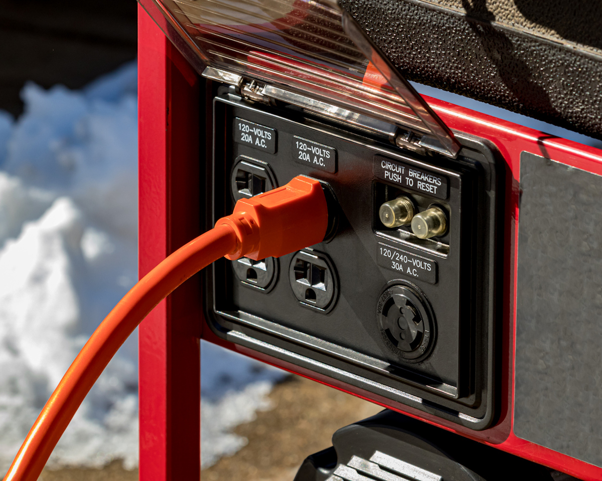 A generator outside in the snow with a cord plugged in.