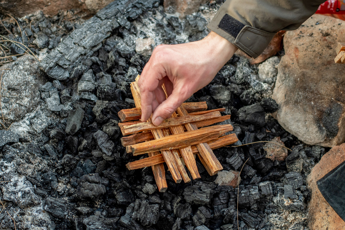 A person is preparing to create a fire by stacking kindling in a cross structure inside of a fire pit.