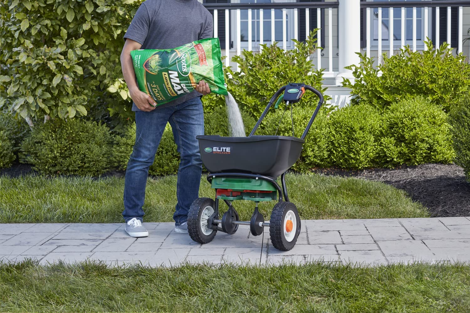 A person pouring a bag of fertilizer into a spreader