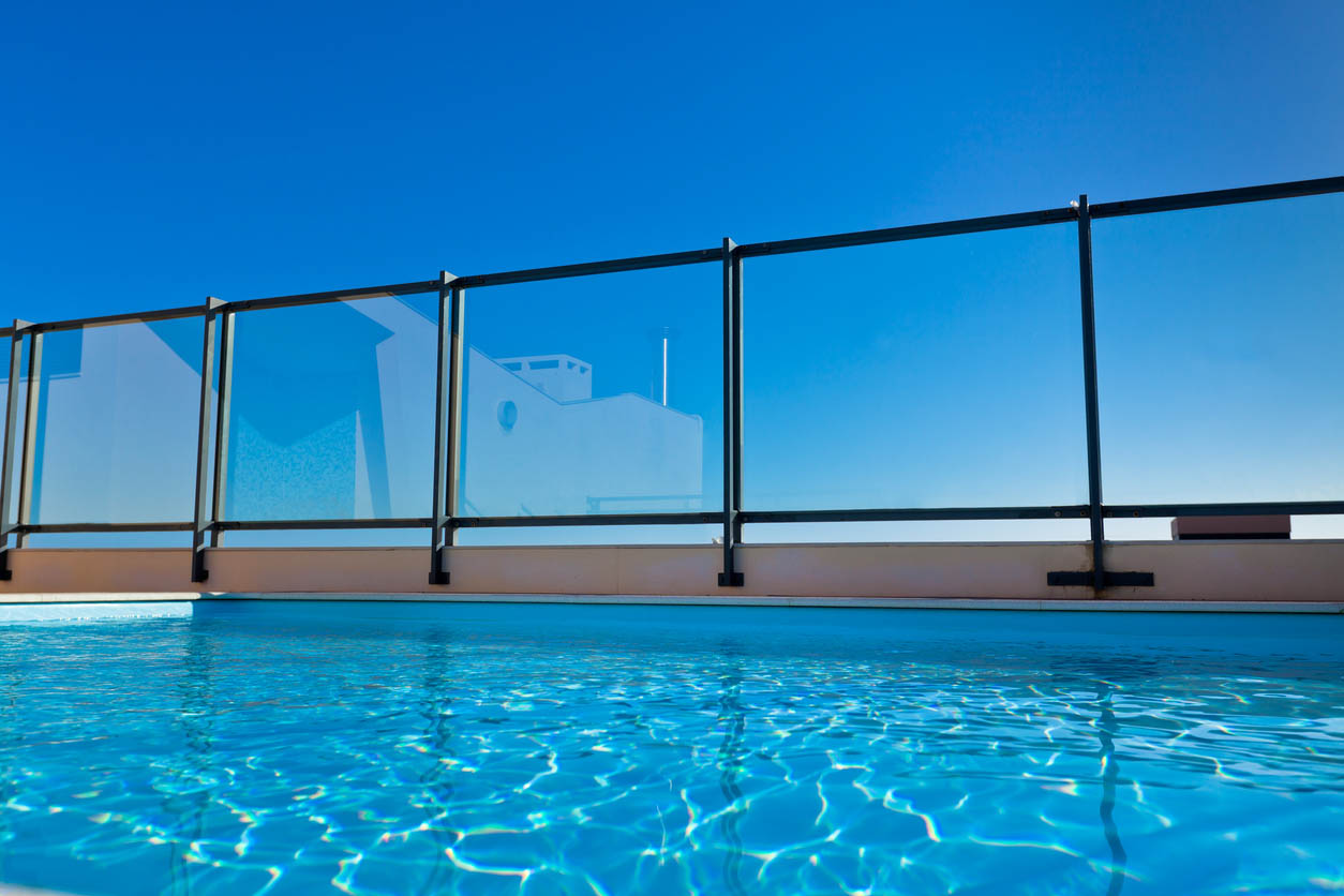 A glass fence surrounds an inground swimming pool.