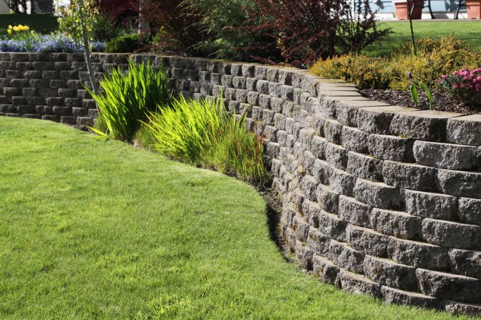 A close up of a retaining wall surrounded by plants and grass.