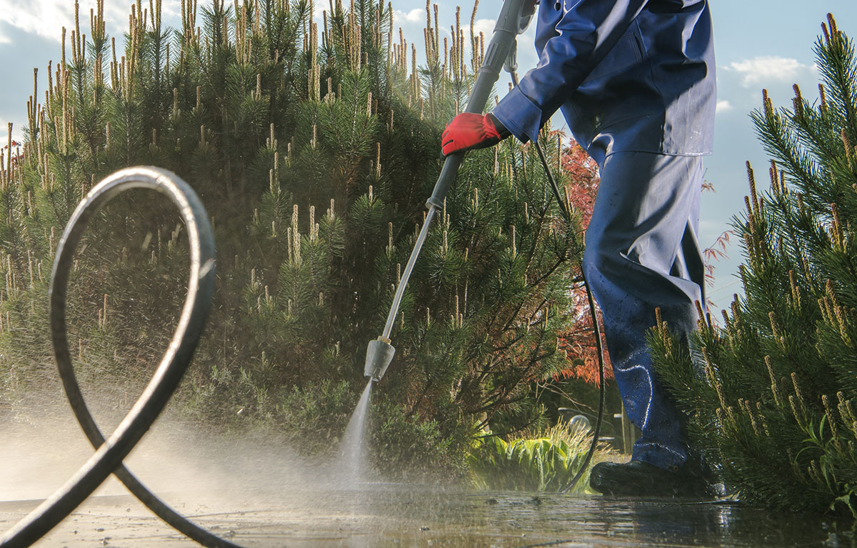 A person wearing protective clothing power-washes an outdoor concrete area.