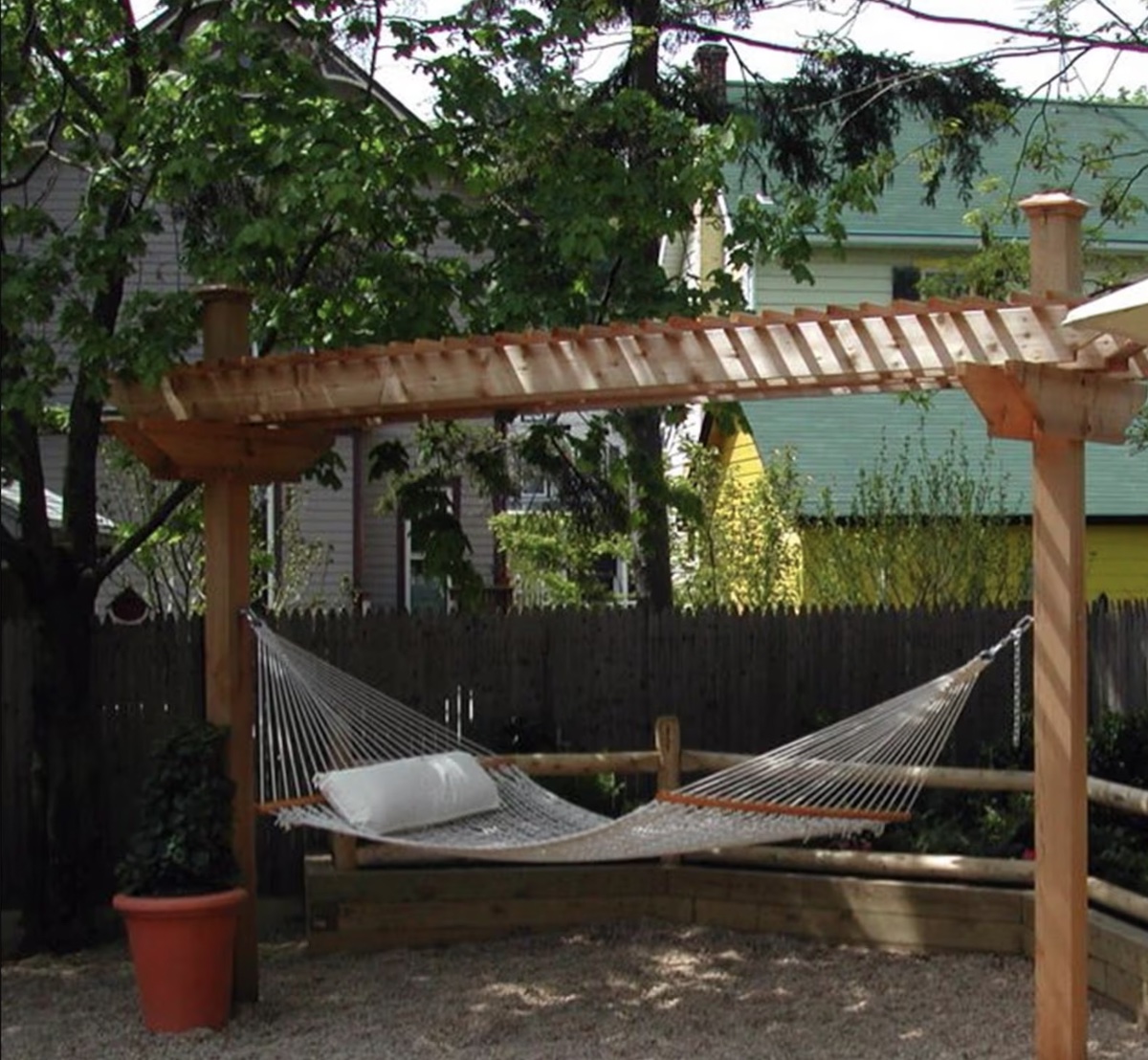 Backyard scene with a hammock hanging from a wood pergola. 