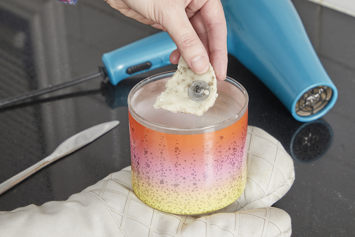 Woman removes wax pieces from candle jar after heating it with a hair dryer.