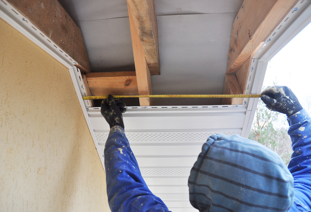 A roofer measures the soffit next to a home.