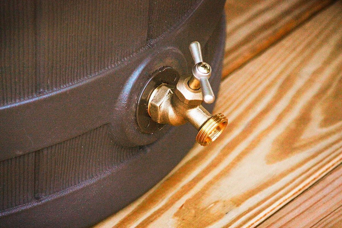 Closeup of a spigot on the bottom of a rain barrel sitting on a wooden floor