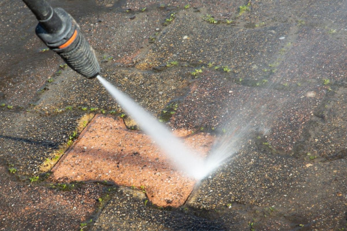A close up of a dirty brick surface being cleaned by a pressure washer.