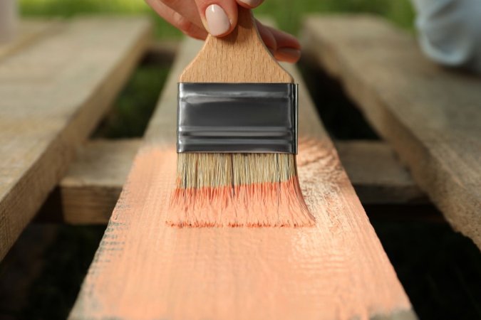 A close-up of a person painting a wooden deck board.