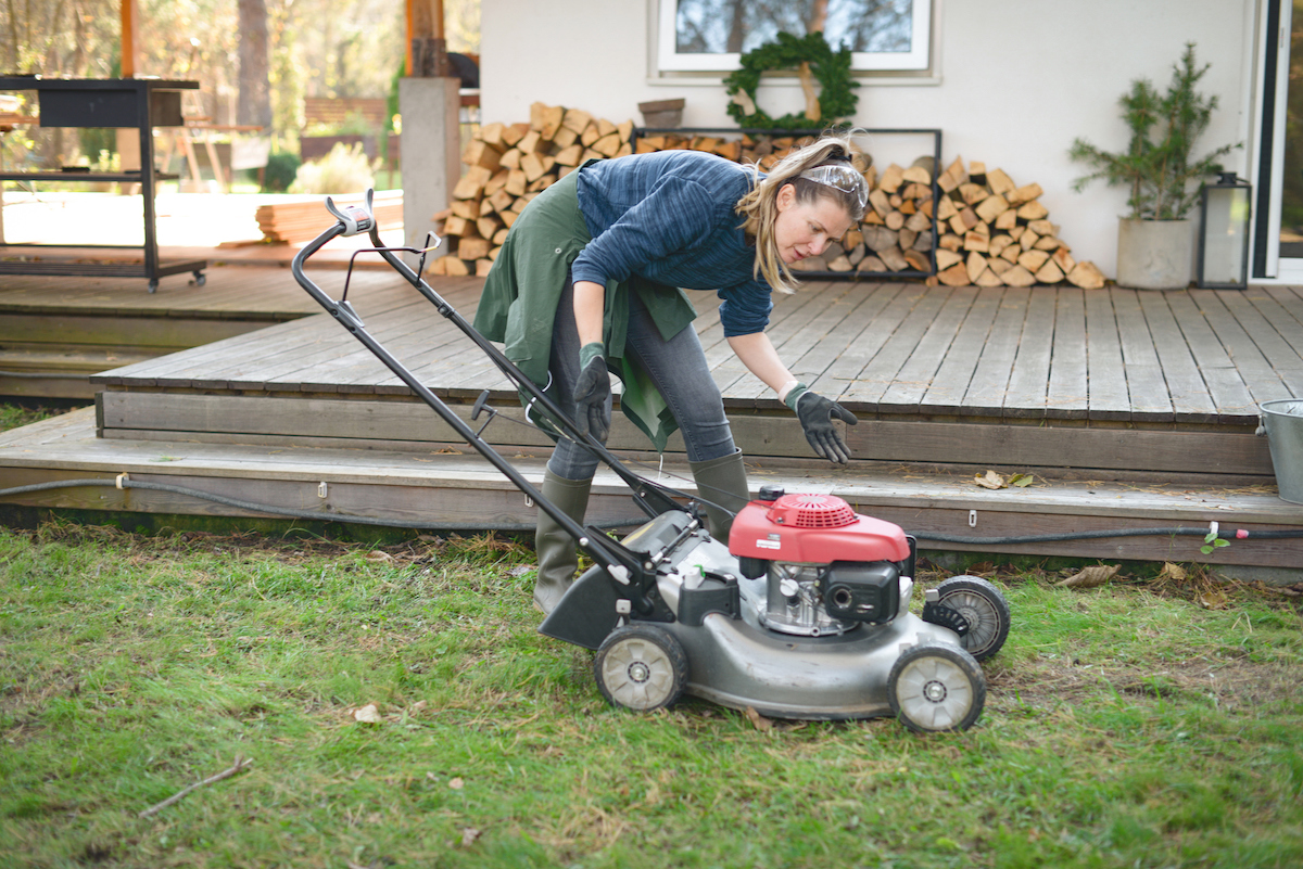 A woman is checking on a lawn mower in a back yard.