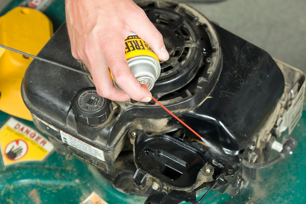 A person is using a can of compressed air to clean the carburetor of a lawn mower.