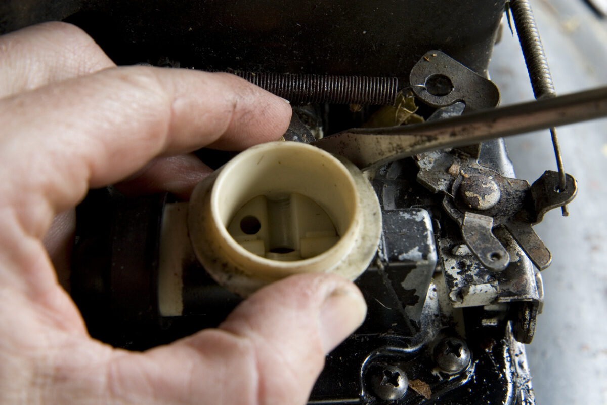 A person's hand is removing the carburetor of a lawn mower in order to clean it.