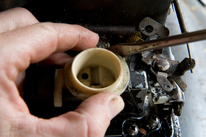 A person's hand is removing the carburetor of a lawn mower in order to clean it.