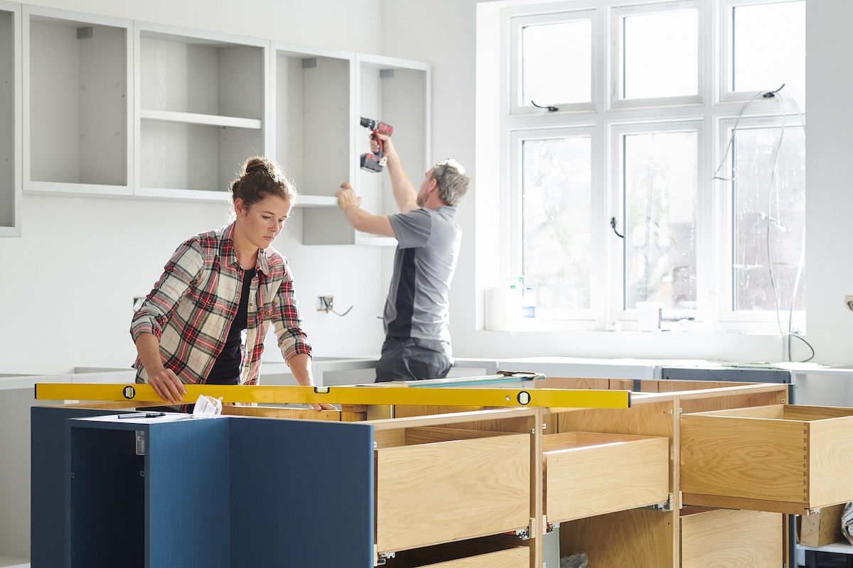 A man and woman measure a kitchen for remodels.