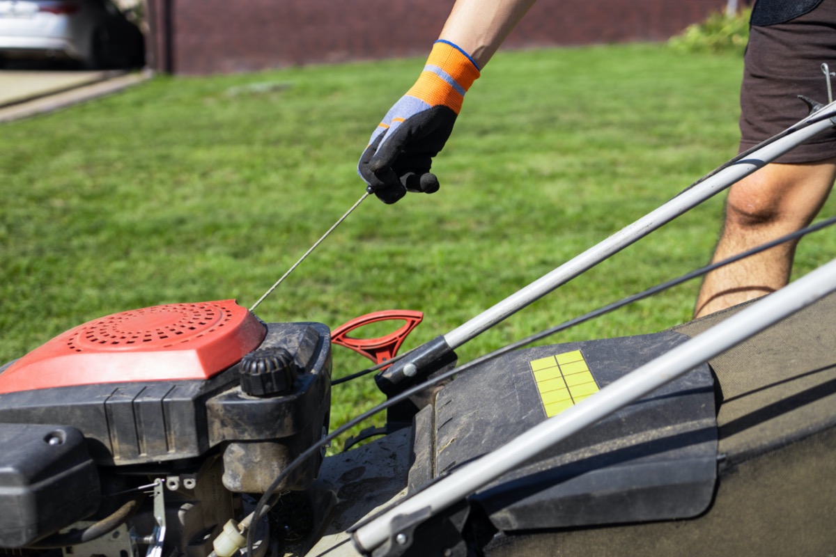 A person wearing a glove is starting a lawn mower with the pull cord.