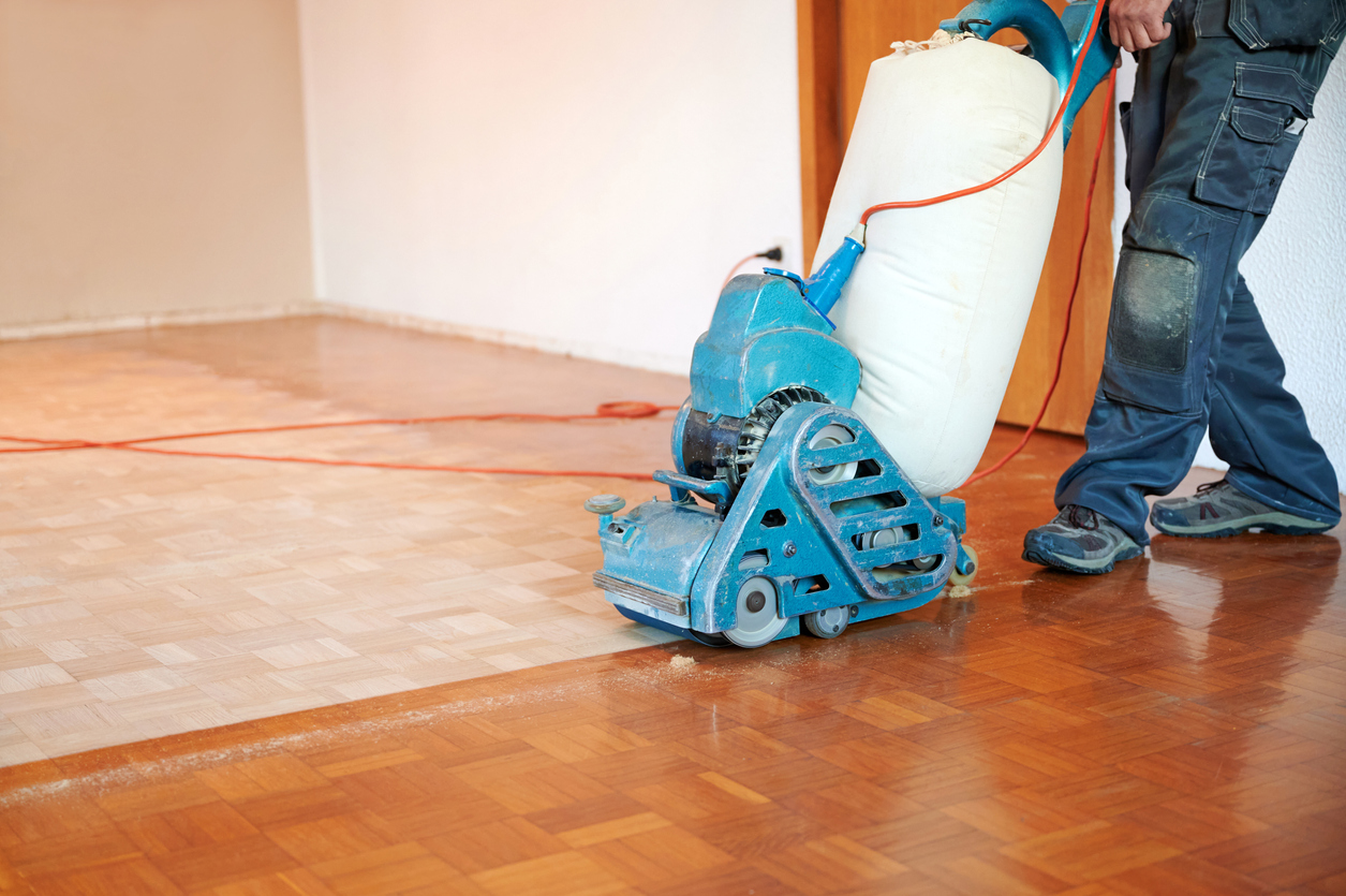 Worker polishing a parquet floor with grinding machine.