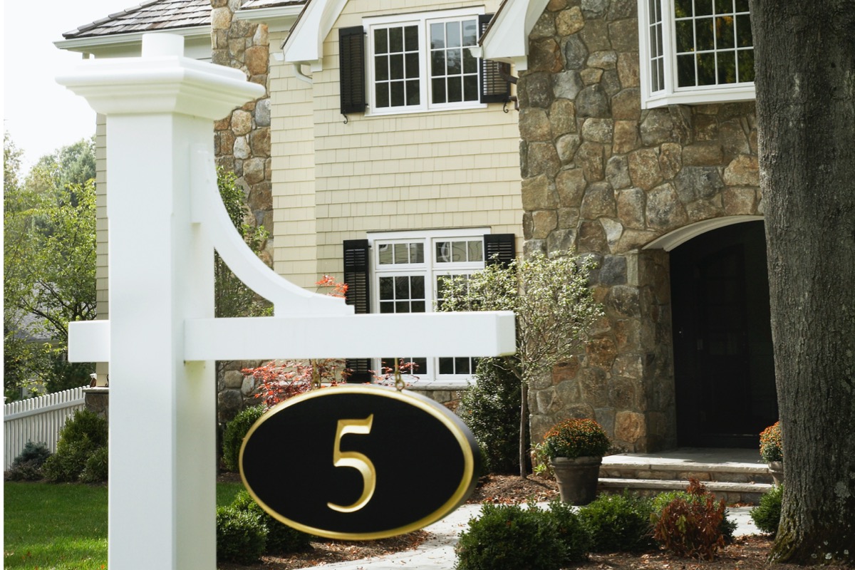 A #5 house number hanging on a white post in front of a big house.