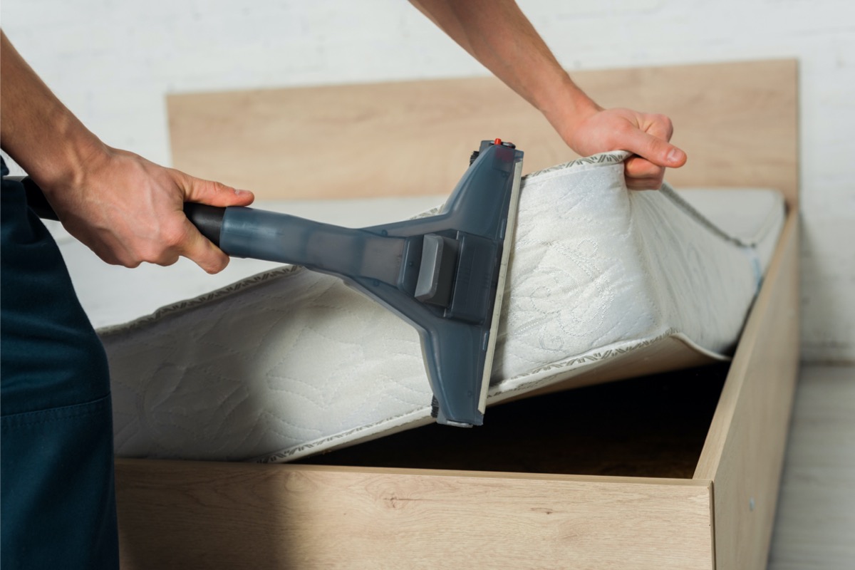 Person vacuuming a mattress with a vacuum attachment.