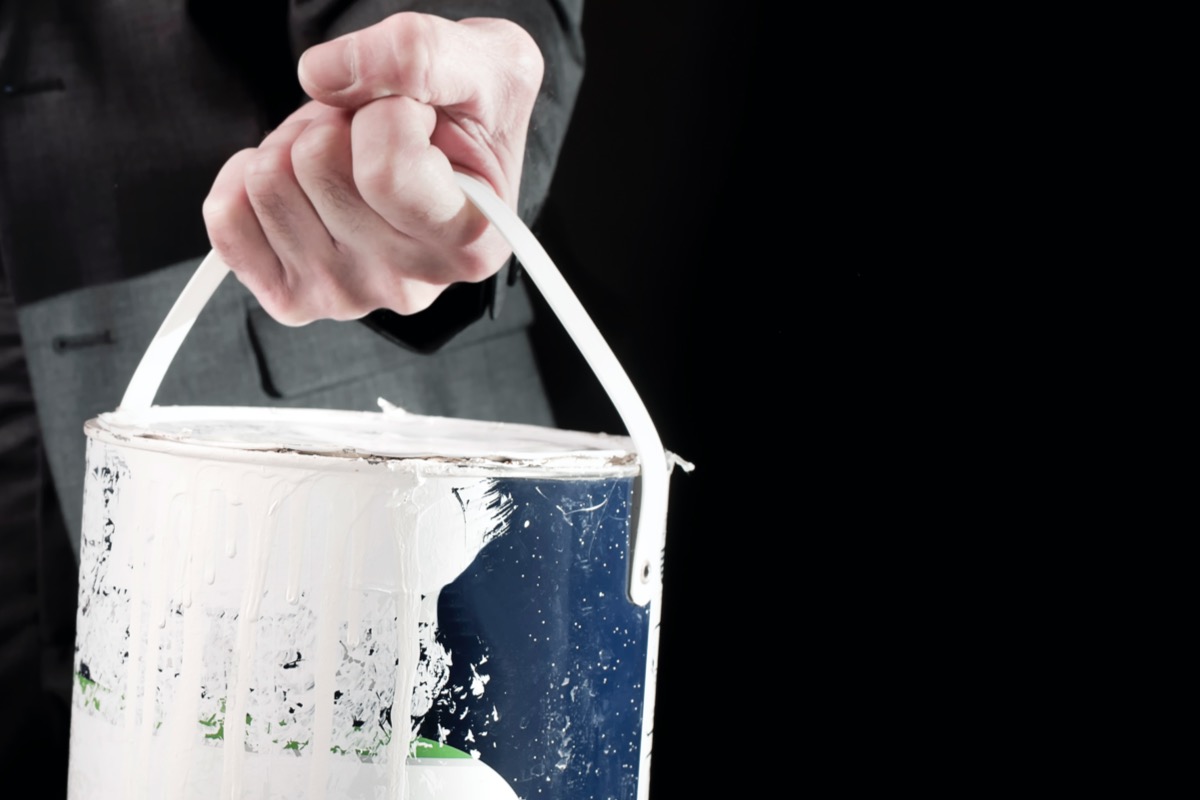 Man carrying an old can of paint with white paint dripping down the side.