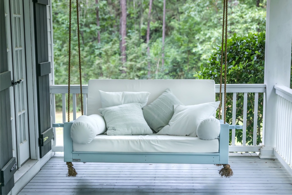 A porch swing with cozy white cushions on a front porch.