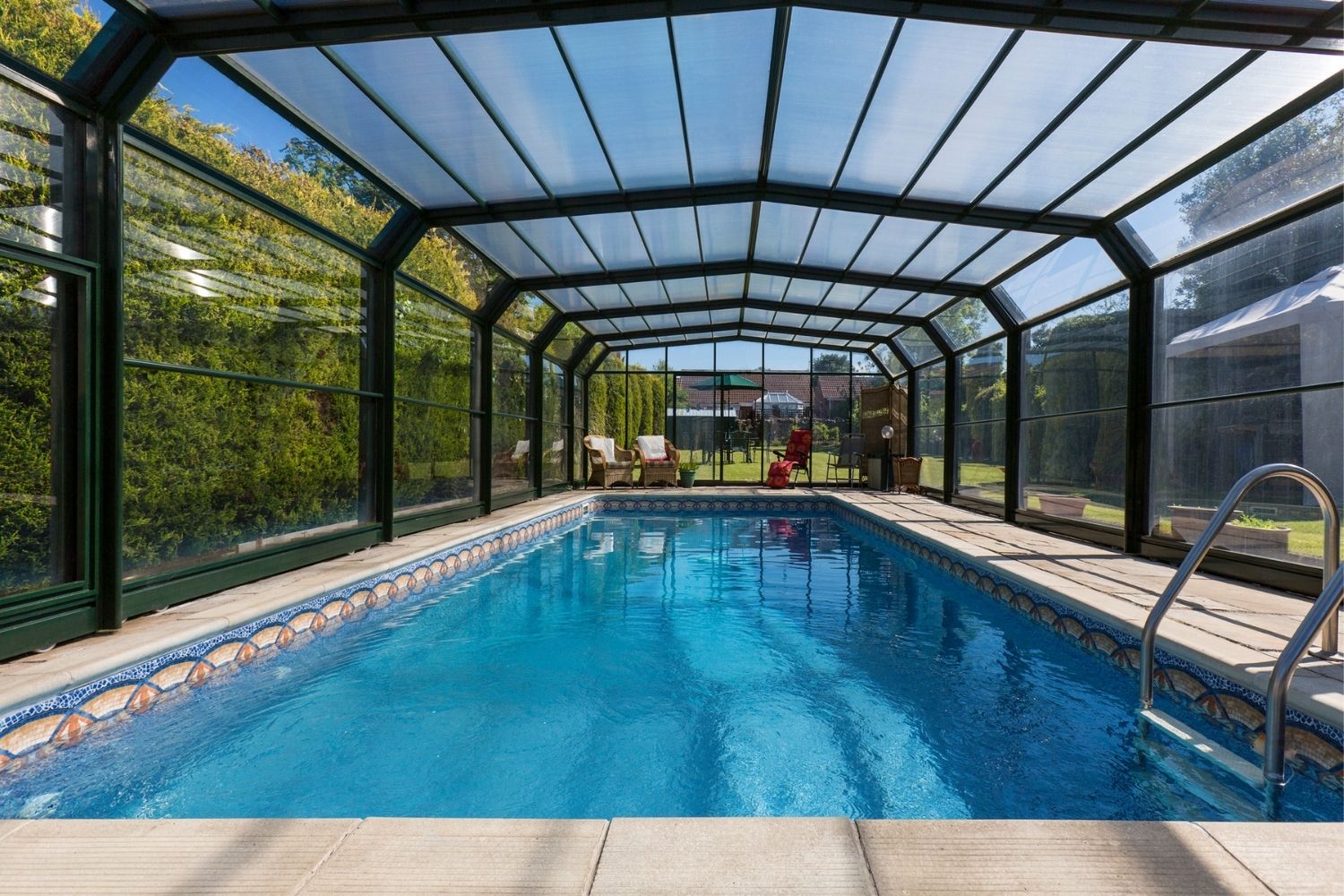 A backyard inground pool with a black-and-glass pool screen enclosure.