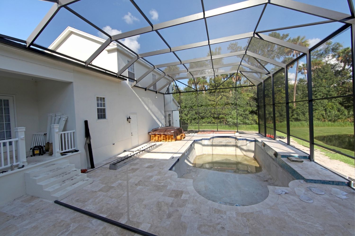 An inground backyard pool half-constructed with a pool screen enclosure connecting it to the home.