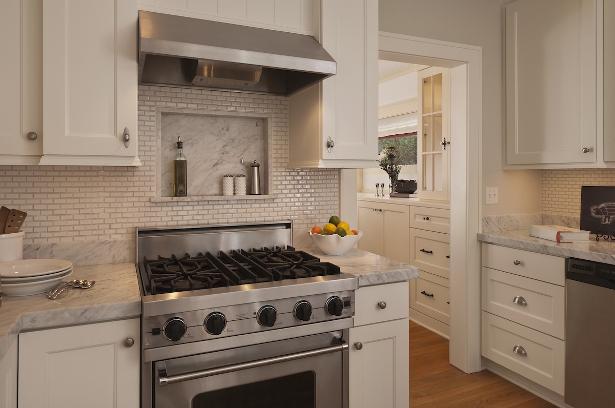 A traditional white kitchen with a stainless steel oven and subway tile backsplash.