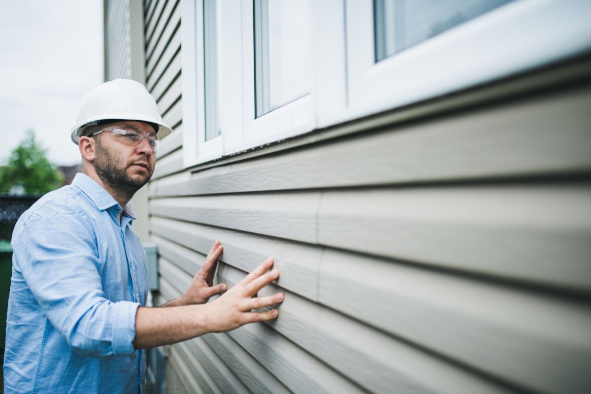 A contractor in a hard hat inspects siding on a house.