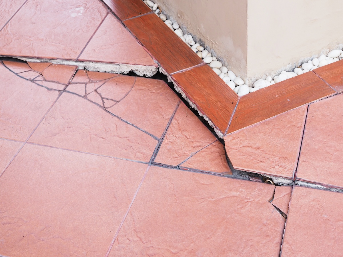 The corner area of tiled floors with cracks in the terra cotta-colored tiles. 