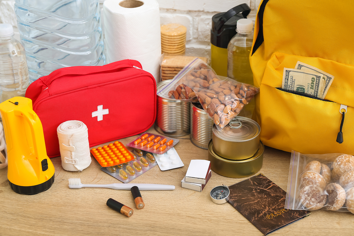 Necessities for emergency bag on wooden table, including first aid kit, medicine, food, and more.