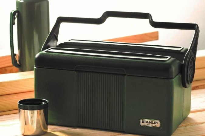 A dark green Stanley lunchbox on a wooden table