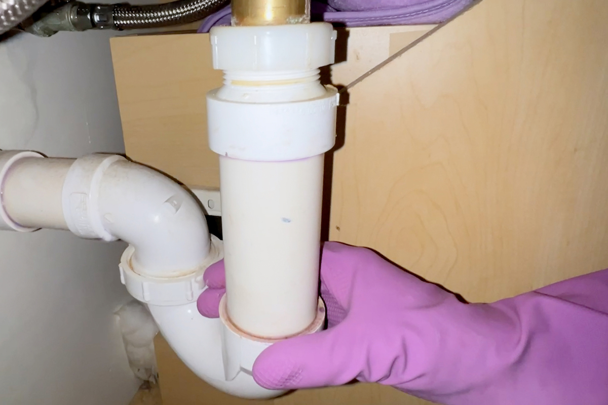 Woman wearing pink rubber gloves checks P trap under sink.