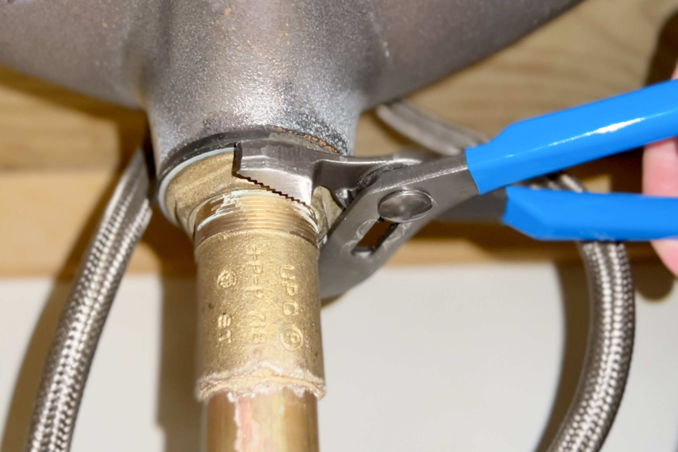 Person uses pliers on pipe under bathroom sink.