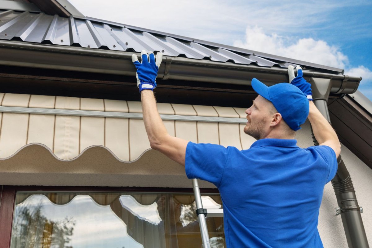 A man dressed in blue installs a gutter guard.