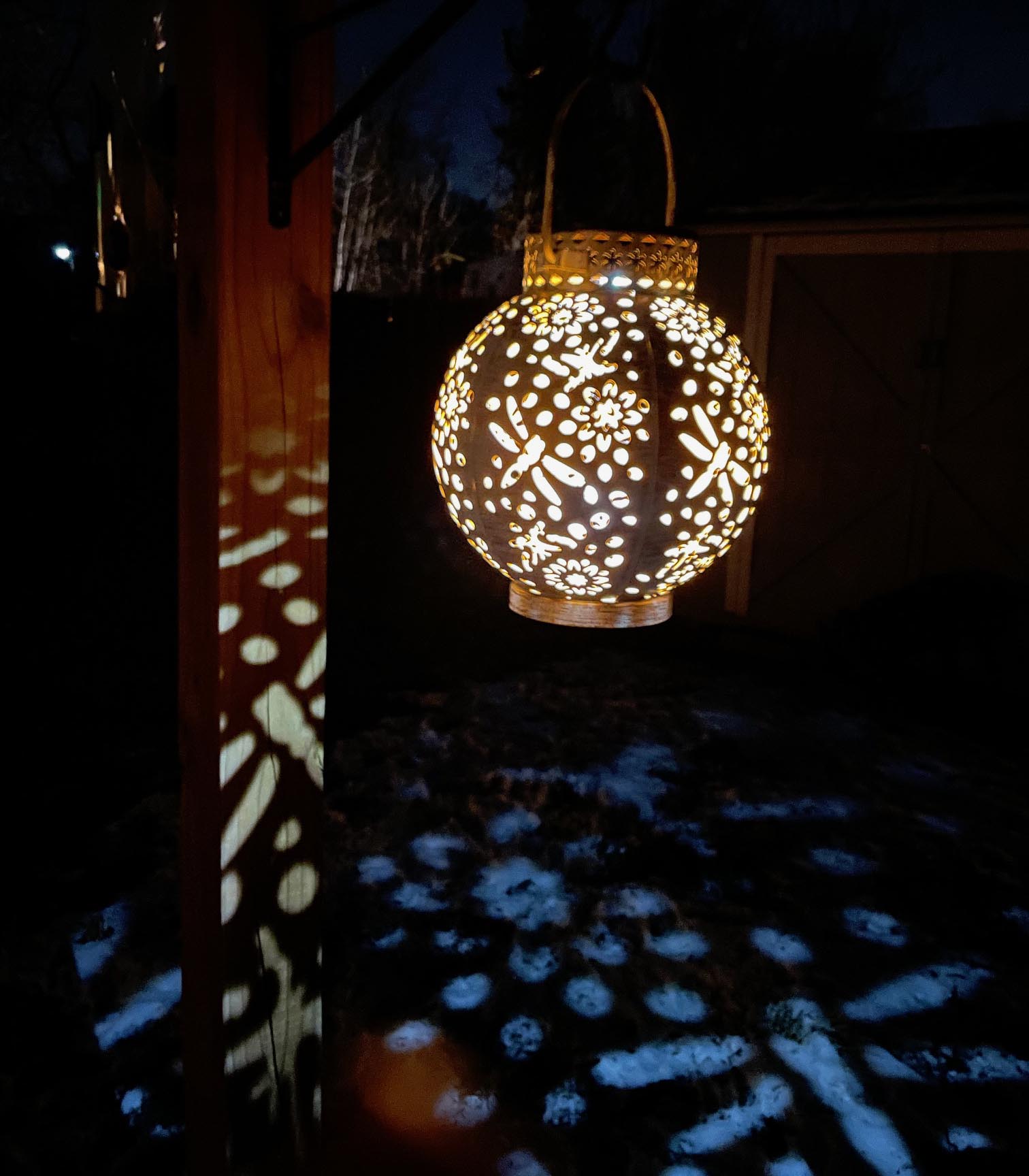 Kooper Solar-Powered Integrated LED Outdoor Lantern hanging from a hook on a deck post lit up at night