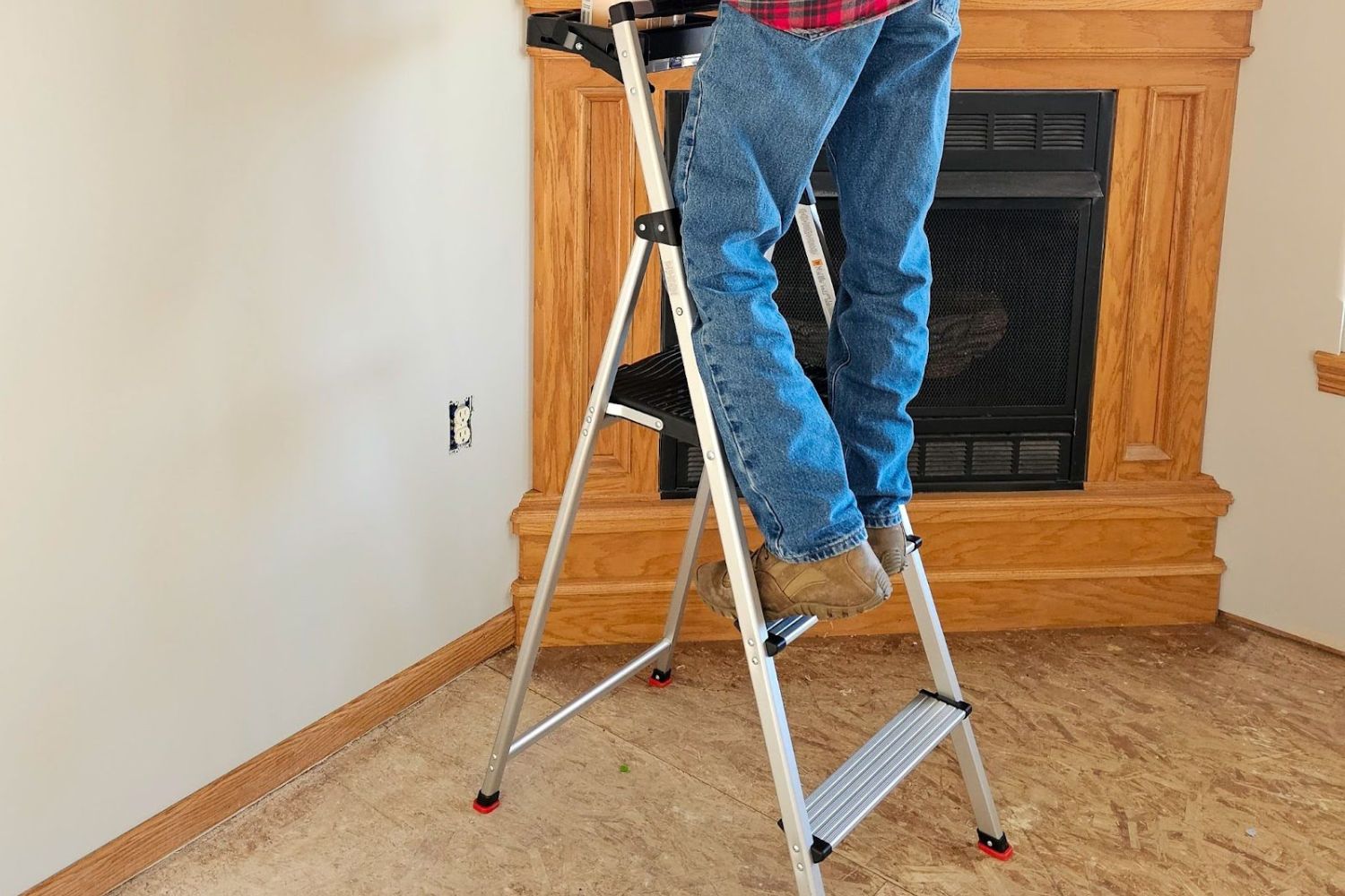 A person on the second step of the Rubbermaid 3-Step Aluminum Stool that has a can of paint on its project tray.