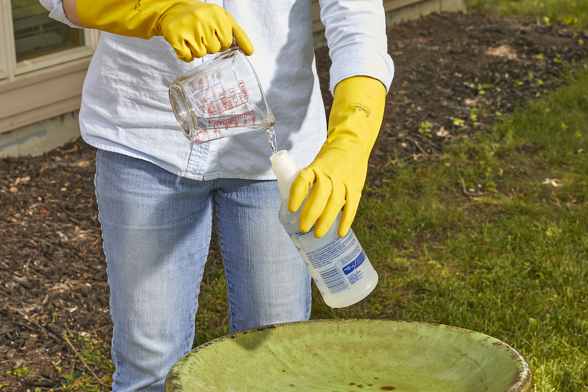 Woman pours vinegar from a measuring cup into a spray bottle.