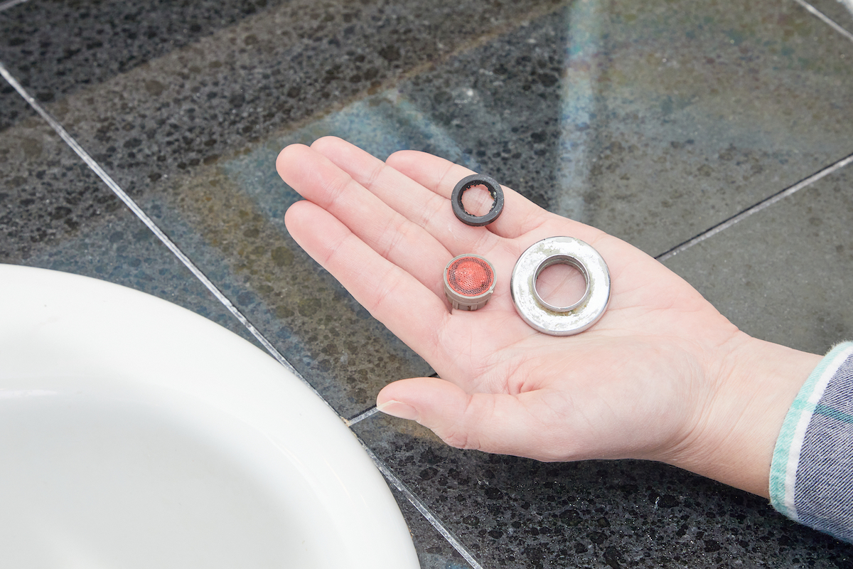 Woman holds the parts of a faucet aerator in the palm of her hand.