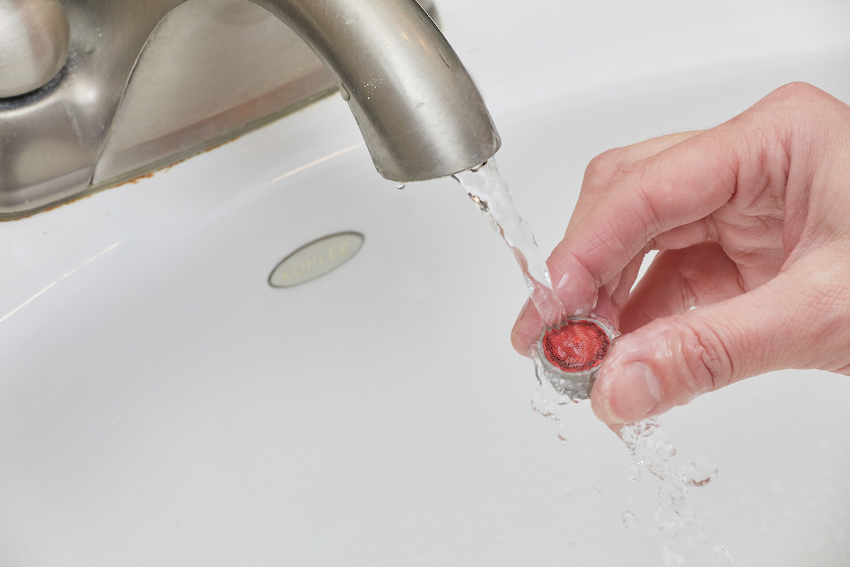 Woman rinses a part of a faucet aerator under a bathroom faucet.