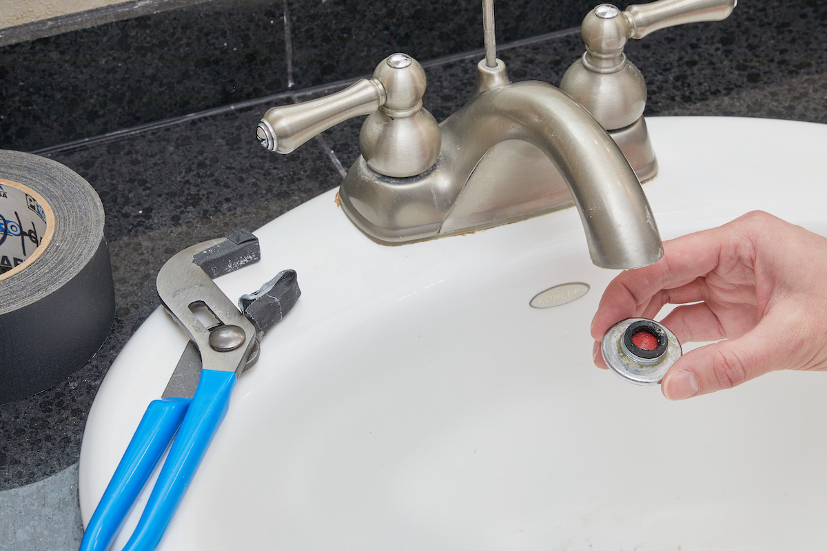 Woman removed faucet aerator from bathroom sink with wrench, which is next to sink.