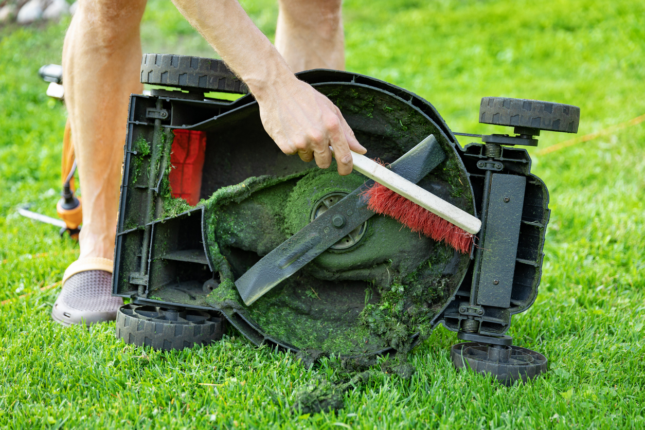 Man cleaning the underside of a lawn mower with a bristle brush.